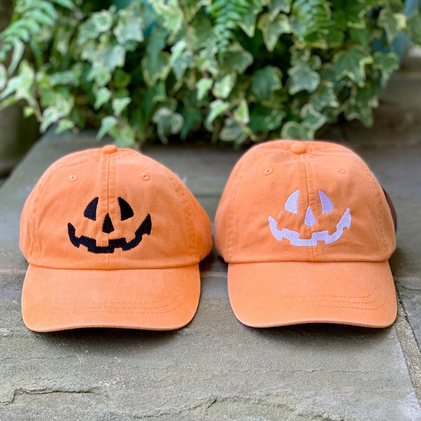 two orange baseball caps with a jack-o-lantern face embroidered in black and one embroidered in white